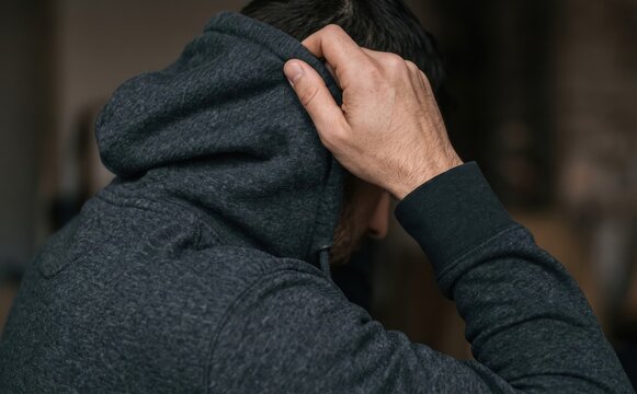 Depressed young Caucasian man wearing a dark hoodie pulling his hood down representing stress and anxiety