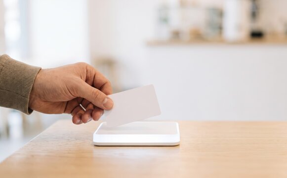 Adult man tapping a white contactless card on a payment terminal on a wooden counter