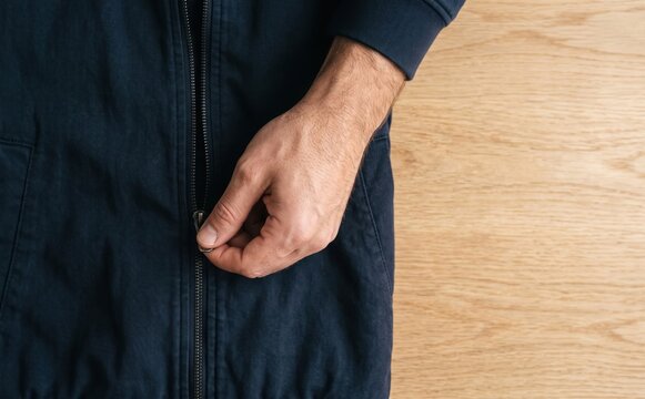 Man zipping dark blue jacket on wooden table close up view representing preparation and dressing