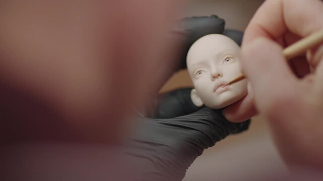 Artist applying fine paint to the face of a female PLA ball jointed doll during the detailed customization process.