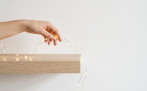 Woman hands decorating wooden shelf with glowing fairy lights for festive interior design