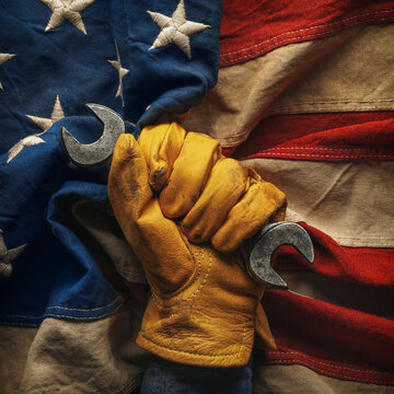 Worn work glove holding wrench on the American flag. Symbolic of hardworking blue collar workers, USA manufacturing, pride in products Made in United States of America, or to celebrate US Labor Day.