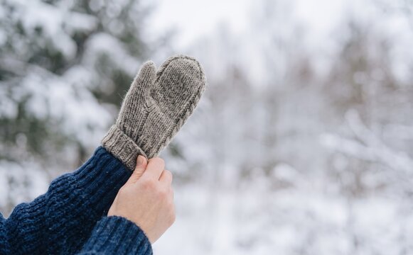 Woman putting on warm knitted woolen mitten in a snowy winter forest outdoors