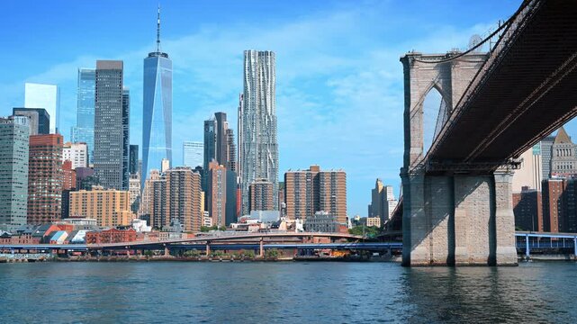 Brooklyn Bridge framing Lower Manhattan skyline. The bridge underside enters from the right above the East River and dense high rises.