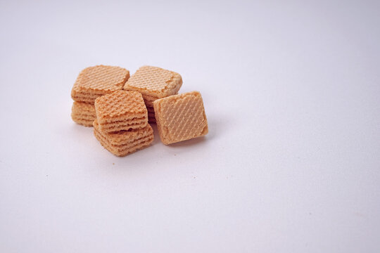 Vanilla waffle cookies stacked neatly on plain surface. Soft, crisp texture hints at delightful crunch. Minimalist backdrop enhances visual appeal. Perfect for food blogs or snack promotion