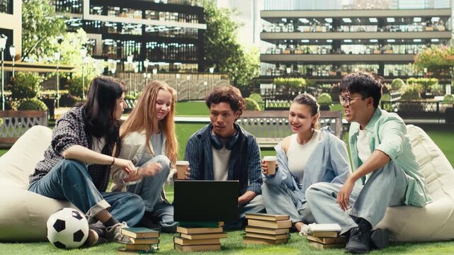 Diverse peers gather on the grass at a university campus for group study session, reviewing coursework notes and sharing ideas together.
