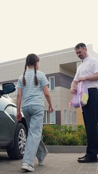father brought daughter school by car, against background school building father puts child backpack, happy family, children education, child goes school lesson, man business suit sees daughter off
