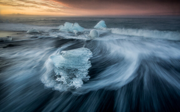 View of ice chunks from Jokulsarlon Glacier Lagoon washing onto the black sand beach at sunset in Hornafjordur, Iceland.