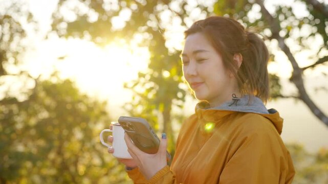 Asian woman remote working corporate business on smartphone with drinking coffee while travel nature forest camping on mountain. Digital nomad people enjoy workation outdoor lifestyle nature therapy