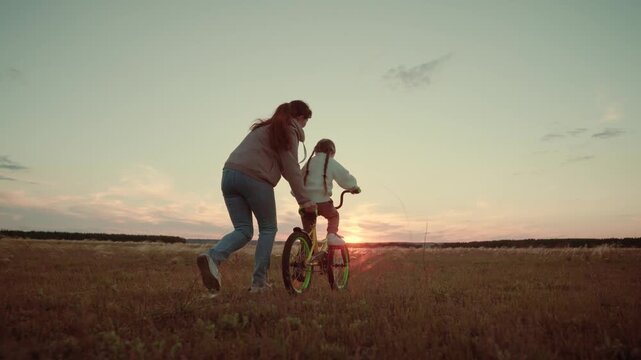 Bike ride at dusk, Mother empowering daughter, Heartwarming scenery, Fun in the field, Parenting moments, Trying something new, Innocent joys, Rural beauty, Evening silhouette, Building trust