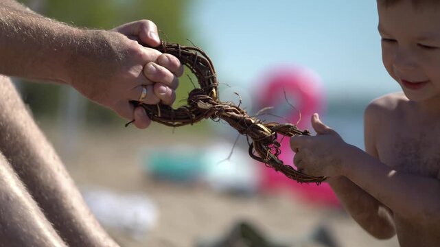 Man and boy child play tug-of-war with thick intertwined roots braided into circles or a chain on sunny sandy beach near water.