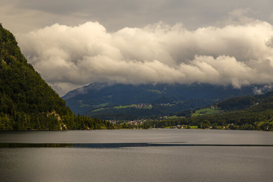 View of a calm lake surrounded by lush green mountains under a dramatic cloudy sky in Hallstatt, Upper Austria, Austria.