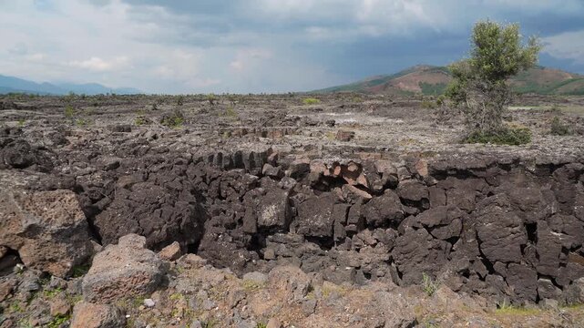 Basalt lava plain with porous volcanic rocks and sparse vegetation forms a harsh landscape.