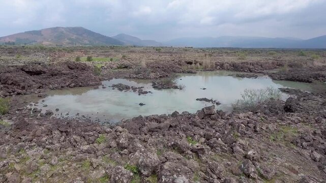 Aerial basalt lava plain with calm lake water and dark volcanic rock reveals a rugged basin.