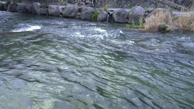 High angle view of a rushing river stream with stone embankment wall and drainage pipe on the opposite bank