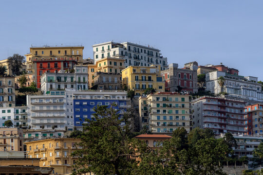 View of colorful historic residential buildings and apartments stacked on a hillside under a clear blue sky in Naples, Campania, Italy.