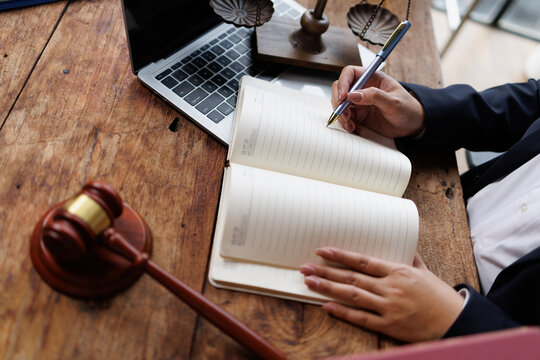 Legal professional writing notes on a notebook with gavel and scales of justice, discussing law and judicial matters