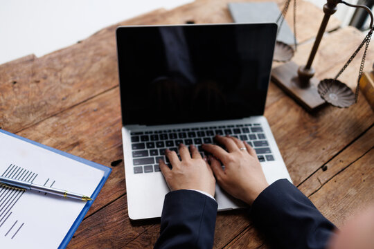 Lawyer hands typing on laptop keyboard, analyzing legal document, justice scale, and law career concept