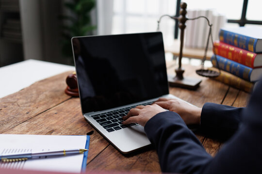 Lawyer working on laptop, typing legal documents, research, and analysis in law office with scales of justice and law books