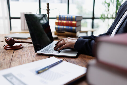 Legal professional typing on laptop at desk with gavel, scales of justice, and law books in a modern office