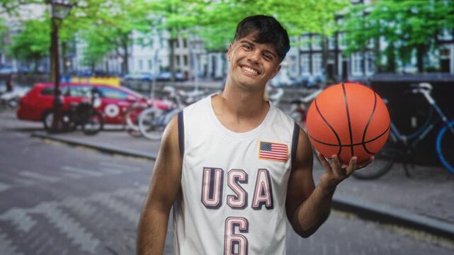 Man holding basketball in hand on street wearing usa jersey number 6 and smiling at camera; confidence playful.