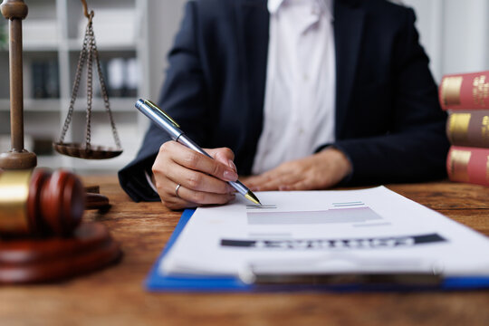 Lawyer or attorney signing legal paperwork on a wooden desk, with a gavel, scale of justice, and law books