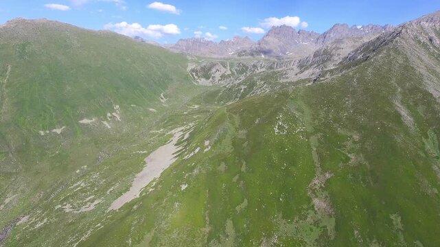 Aerial u shaped valley with stream and green meadows spans treeless alpine terrain.