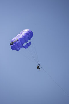 View of people parasailing with a purple parachute against a clear blue sky in Zakinthos, Greece.