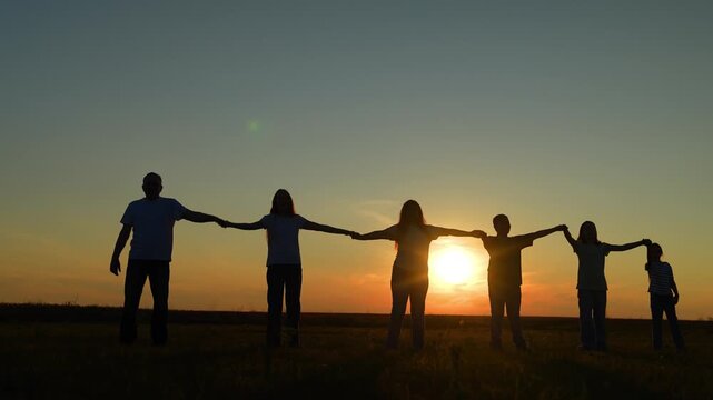 golden hour togetherness: family and friends holding hands, family group support and team spirit outdoors, silhouettes of togetherness against a fiery evening sky, loving parents guiding children