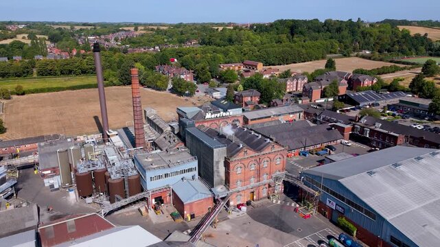 Historic brick brewery building with smokestacks and green fields backdrop