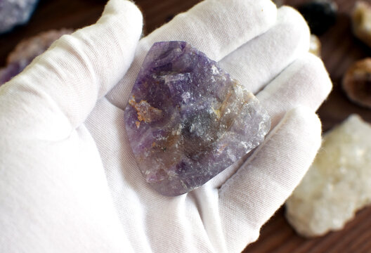 A hand in a white glove holds a purple fluorite against a background of gemstones