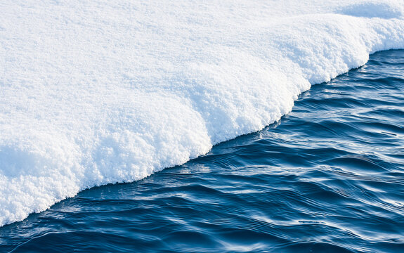 Close-up abstract view of textured frozen ice formations bordering rippling cold blue water