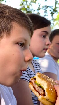 school children eat big hamburger, kids eat burger park, group children friends eat cutlet bun, Outdoor Food Adventure, Youngsters Feasting Together, Parkside Burger Meal, Laughter and Lunch, Children