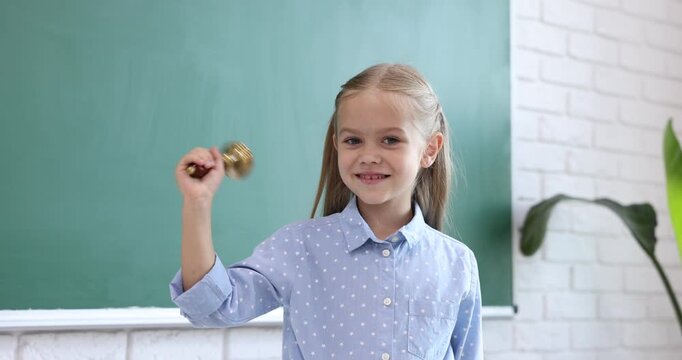Little girl ringing school bell in classroom