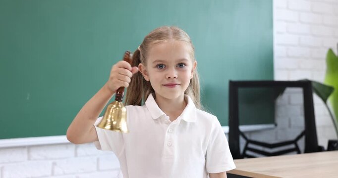 Little girl ringing school bell in classroom