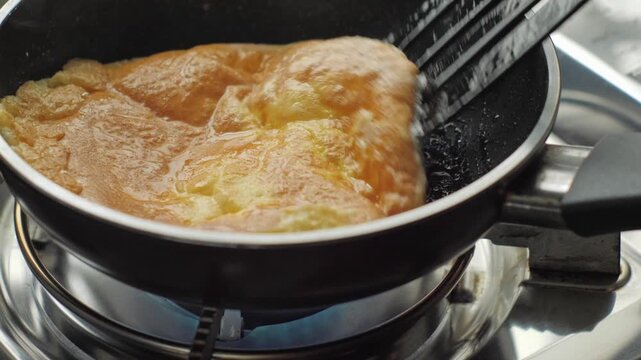 Close-up of a homemade omelet being flipped in a frying pan, capturing an authentic home cooking moment with natural kitchen sound.