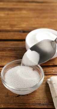 Pouring baking soda into bowl with water at wooden table, closeup