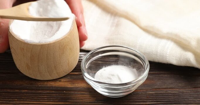 Woman pouring baking soda into bowl at wooden table, closeup
