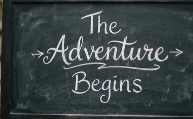 Fototapeta premium Chalkboard sign with handwritten text The Adventure Begins inspiring travel and journey concepts for creative projects