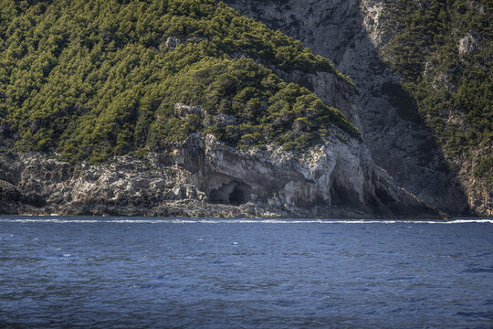 View of sea caves carved into the rugged limestone cliffs covered with lush green vegetation along the coastline of Zakynthos, Greece.