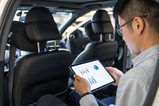 A man in a car uses a tablet to analyze data charts and graphs for business work.