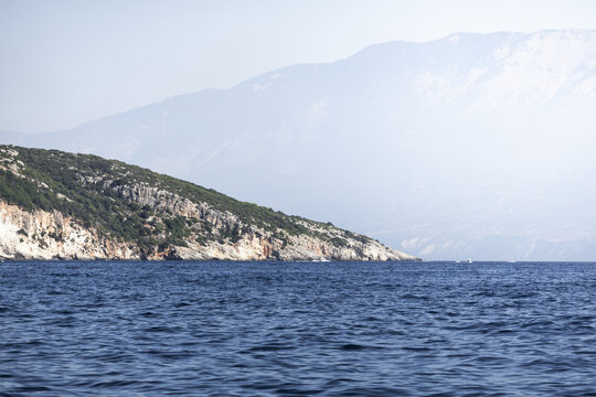 View of the rugged coastline and steep cliffs of Zakinthos rising from the deep blue Ionian Sea under a hazy sky, Zakinthos, Greece.
