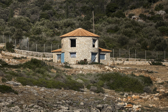 View of a traditional stone windmill house with a conical roof and blue doors set against a rocky hillside in Zakinthos, Greece.