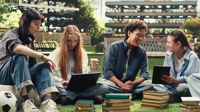 Diverse students check notes on tablet and laptop with a stack of books during outdoor campus study, sharing ideas for a collaborative academic project.