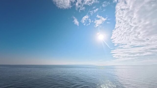 Cinematic real-time wide angle video of bright sun and vivid cloud boundary over sparkling ocean