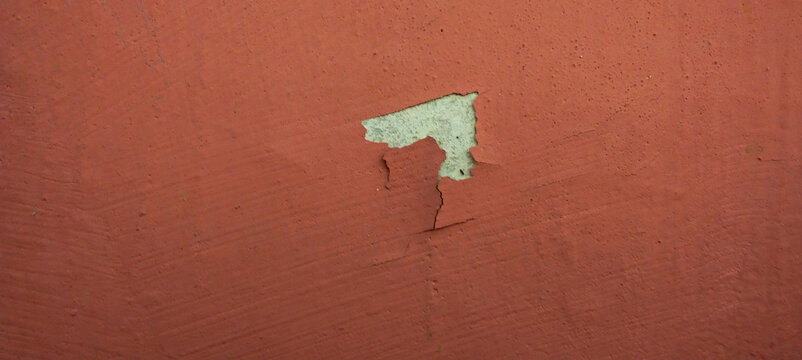 Peeling red wall paint revealing the base layer.