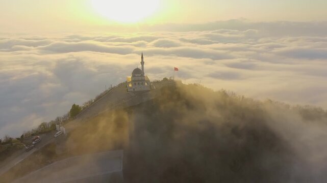 Aerial mosque and minaret above sea of clouds at sunrise during Ramadan, serene prayer scene.