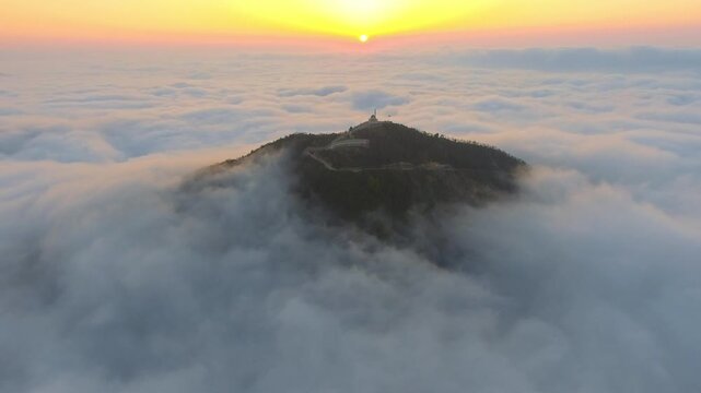 Aerial mosque and minaret above sea of clouds at sunrise during Ramadan, serene prayer scene.