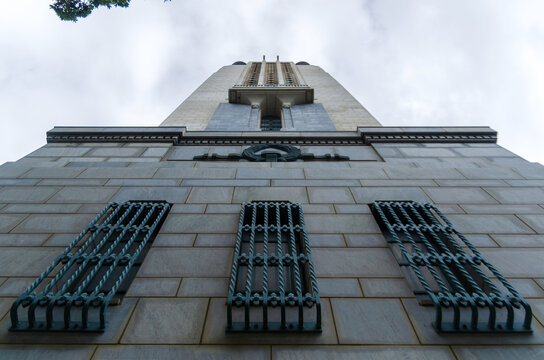 A dramatic upward perspective of a stone memorial tower highlights its ornate windows and crest against an overcast Wellington sky