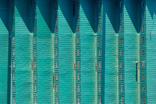 Aerial view of the teal-colored corrugated metal roof of an industrial building in Belgrade, Serbia, with a rhythmic pattern of ribs and small windows casting shadows.